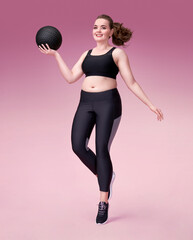 Sporty girl with medicine ball in motion. Photo of model with curvy figure in fashionable sportswear on pink background. Dynamic movement. Sports motivation and healthy lifestyle