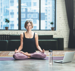 Woman Sitting in Lotus Pose. She is Calm, relaxed and happy outside the window bustling metropolis. Yoga Female Practicing Yoga Meditation Exercise on Mat in her Living Room at Home. Close-up