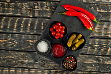 Ketchup and spices on a cutting board. Pickled cucumbers, tomatoes, sauce, salt, pepper and spices on an old shabby table. Copy space and free space for text near food.