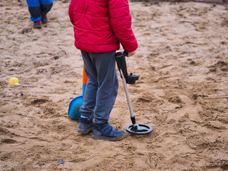 a boy in a sandbox looking for treasure with a metal detector