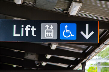 A black Direction sign pointing to the lift with disabled access.