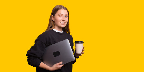 Photo of beautiful girl carrying laptop and hold a cup of coffee over yellow background