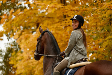 Beautiful brunette on a horse on the background of an autumn landscape. Horseback riding, active horseback riding
