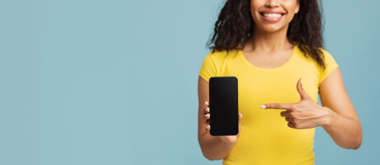 Choose this. Happy african american woman pointing on blank phone screen on blue background,...