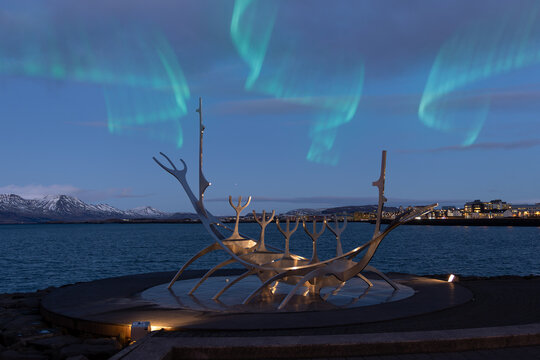 Reykjavik, Iceland. 12.22.2021. Reykjavik's symbol, the "Sun Voyager" steel sculpture against the backdrop of the city at night, snow-capped mountains and the northern lights