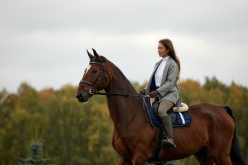 Beautiful young woman riding a horse on the field. Sideways to the camera. Freedom, joy, movement