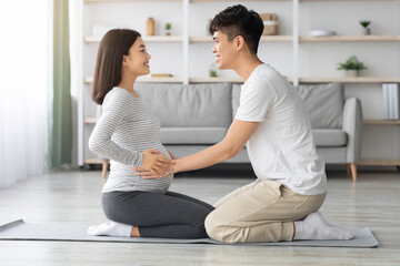 Young asian man helping his pregnant wife exercising