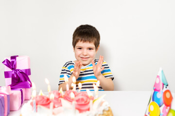 A handsome preschool boy with a cake on his birthday claps his hands on a white background.