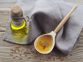 Flaxseed oil in a wooden spoon,oil in a bottle and linseeds with a linen napkin on a wooden background, top view. Natural healthy oleum lini with omega and vitamins for vegetarian diets