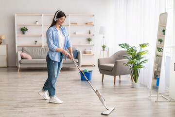 Cheerful woman listening to music cleaning floor with mop