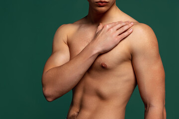 Cropped portrait of young handsome shirtless sportive man isolated on green background. Muscle male...