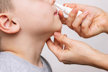 A close-up of female hands using nasal spray for a child's runny nose and congestion isolated on a...