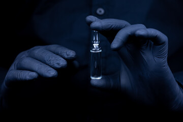 the hands of a medical worker in black medical gloves hold showing a closed ampoule with a vaccine