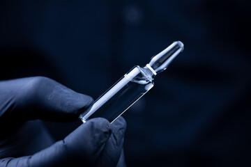 the hands of a doctor in black medical gloves who turns over an ampoule with a vaccine