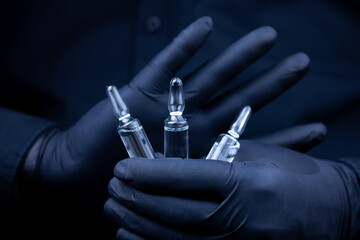 the doctor's hands in black medical gloves holds three vials of vaccine in front of him