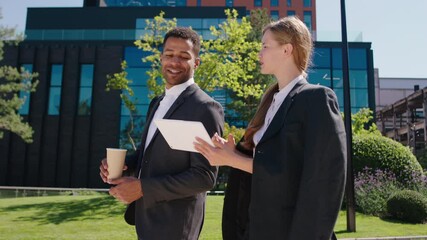 In a perfect sunny day charismatic lady office worker and her colleague black man walking together down the street at the break time discussing together beside modern business centre on the background