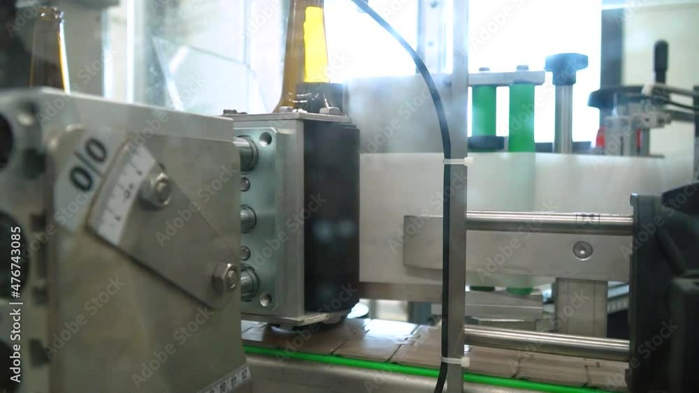 Poster close up of automatic labeling machine at work with empty bottles moving on conveyor in a bottling f