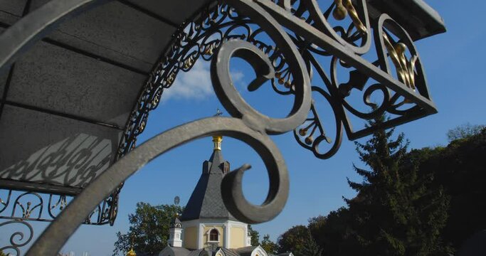 A beautiful view of the Orthodox Christian Church in the monastery, built on a hill covered with conifers on a sunny day, against the backdrop of a cloudless sky.