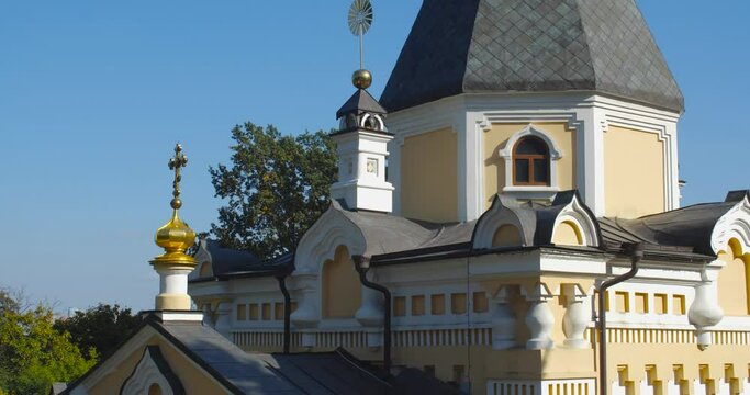 A beautiful view of the Orthodox Christian Church in the monastery, built on a hill covered with conifers on a sunny day, against the backdrop of a cloudless sky.