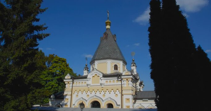 A beautiful view of the Orthodox Christian Church in the monastery, built on a hill covered with conifers on a sunny day, against the backdrop of a cloudless sky.