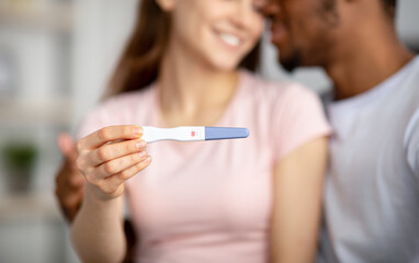 Closeup of happy young multiracial couple showing positive pregnancy test at camera, happy to have...