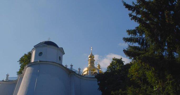 A beautiful view of the Orthodox Christian Church in the monastery, built on a hill covered with conifers on a sunny day, against the backdrop of a cloudless sky.