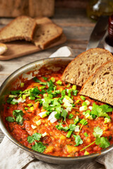 Homemade vegetarian stew with beans, vegetables and cilantro in a frying pan on a gray wooden culinary background close-up