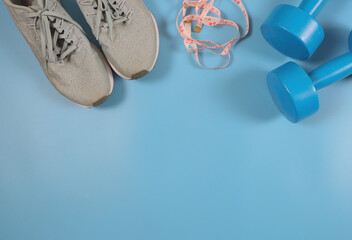 flat lay of grey sneakers , measure  tape and blue dumbbells on blue background. healthy lifestyle and weight loss concept.