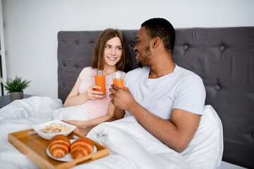 Obraz na płótnie Canvas Loving multiracial couple having breakfast in bed together, spending honeymoon morning at hotel