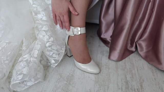 Young woman bride wears white wedding shoes with heels. A girl in a wedding dress gets dressed in the morning before the ceremony.