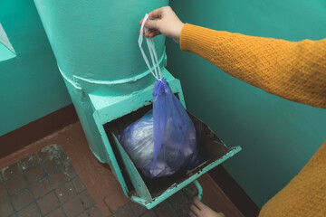 A woman's hand with a garbage bag opens the hatch of the garbage chute and throws garbage there....