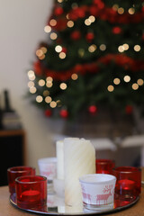 Red and white candles on table in front of Christmas tree.