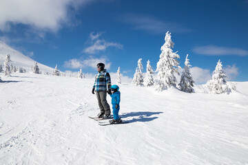 Happy little toddler boy learning skiing with his dad during winter holidays in snowy mountains on sunny cold day