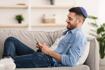 Smiling jew man using mobile phone sitting on couch