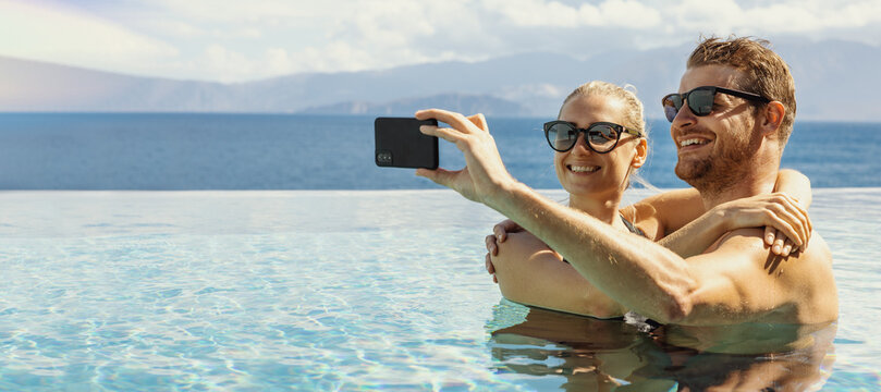 summer vacation - young happy couple taking selfie with phone in resort swimming pool. banner copy space - Powered by Adobe