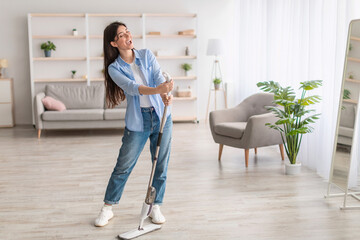 Portrait of cheerful woman cleaning floor singing holding mop