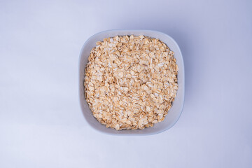 Healthy breakfast. Dry rolled oatmeal in bowl isolated on white background. Top view. Concept of healthy lifestyle, healthy eating, dieting, sport and fitness menu