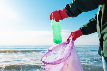 A volunteer wearing rubber gloves puts a dirty plastic bottle in a garbage bag. In the background...