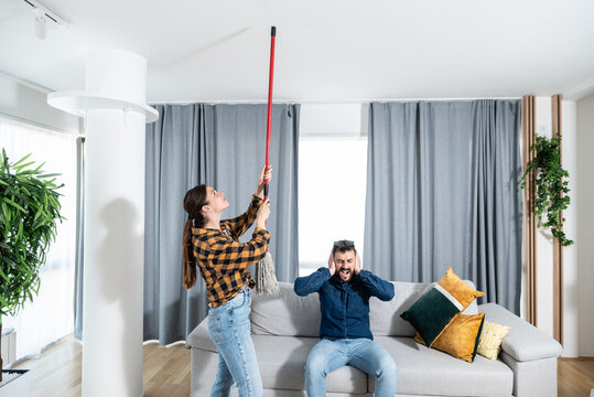 Young couple stares at the ceiling and yells because a neighbor upstairs is having a party with loud music or renovating an apartment and workers are drilling with heavy tools. Nise pollution concept