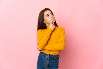 Little girl isolated on pink background having doubts while looking up