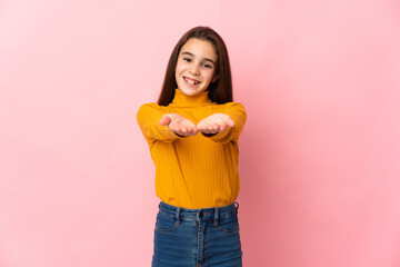 Little girl isolated on pink background holding copyspace imaginary on the palm to insert an ad