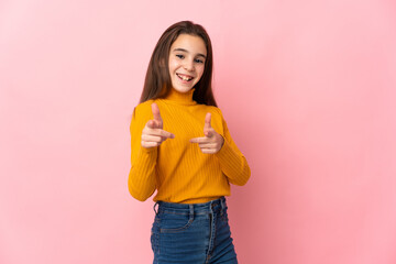 Little girl isolated on pink background pointing to the front and smiling