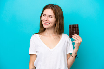 Young English woman with chocolat isolated on blue background looking to the side and smiling