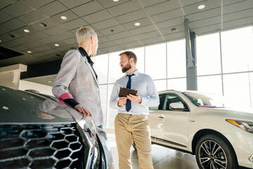Salesman at the dealership showroom talking with customer and helping her to choosing a new car for...