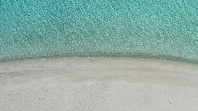 Aerial pull out view of a sandy beach. People relaxing sun shades and calm turquoise water, summer sunny day.