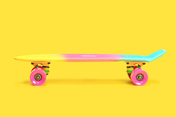 Pastel neon rainbow colored Penny board skateboard isolated on solid yellow background. Plastic mini cruiser. Youth minimalistic Sport inspired summer fun concept. Copy space.