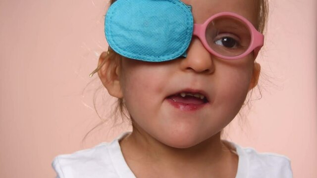 Baby girl 3 years old wearing glasses and an eye occluder  to prevent astigmatism, amblyopia and strabismus (squint, lazy eye).  She smiles. Close-up.