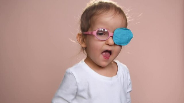 Baby girl 3 years old wearing glasses and an eye occluder  to prevent astigmatism, amblyopia and strabismus (squint, lazy eye). She is happy.