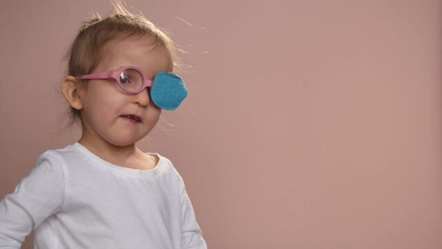 Baby girl 3 years old wearing glasses and an eye occluder  to prevent astigmatism, amblyopia and strabismus (squint, lazy eye). She's clapping her hands a nd smiling. Copy space.
