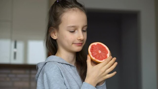 Little girl with long hair is licking a half of the orange. Happy childhood, healthy eating